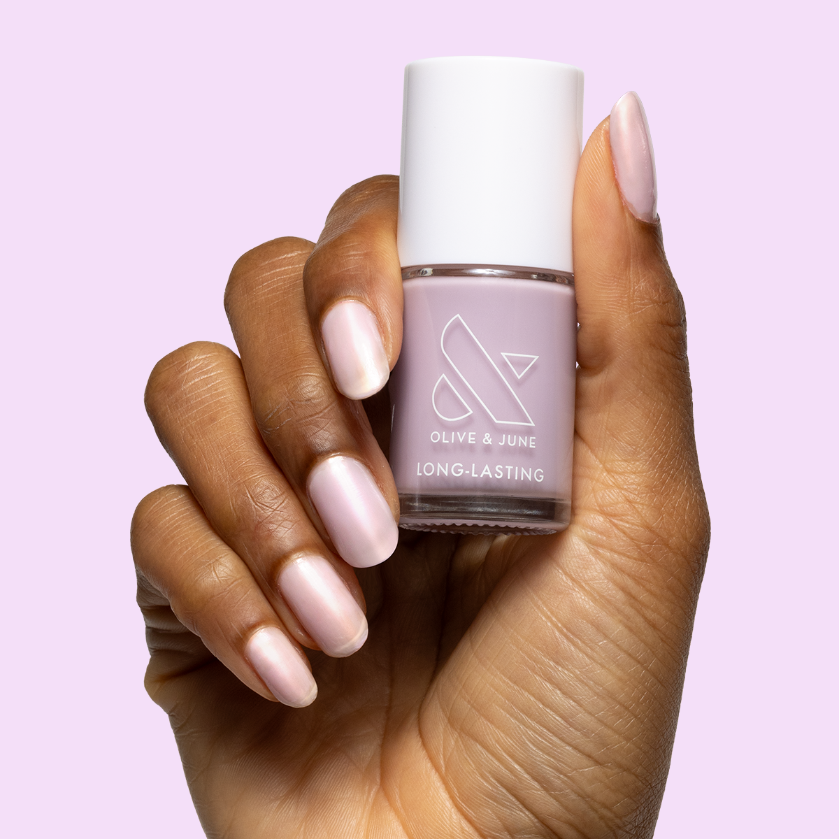 Hand with medium-length nails painted in milky lavender using Passionfruit Gloss polish holding matching bottle on lavender background