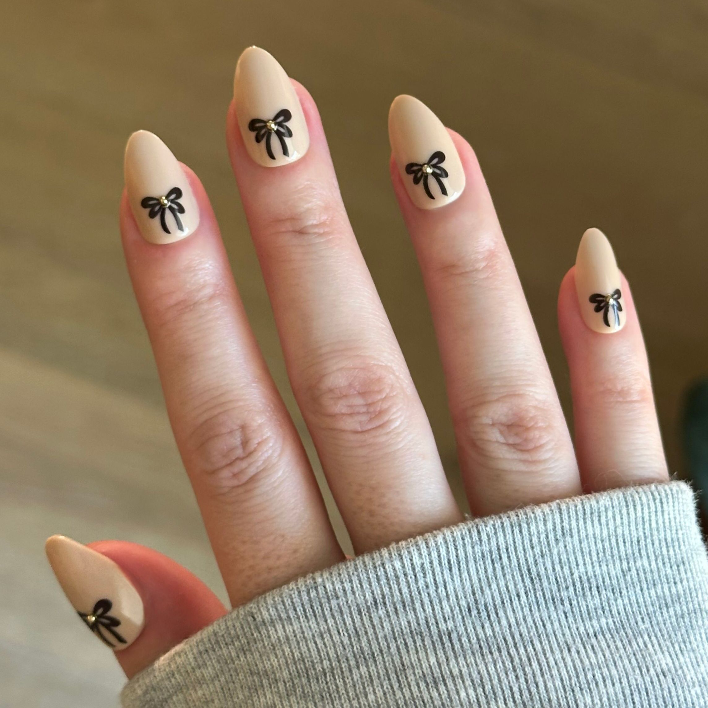 Little Gem Bows - Press On | Medium | Almond with creamy beige nails and black bow designs for a stylish at-home mani
