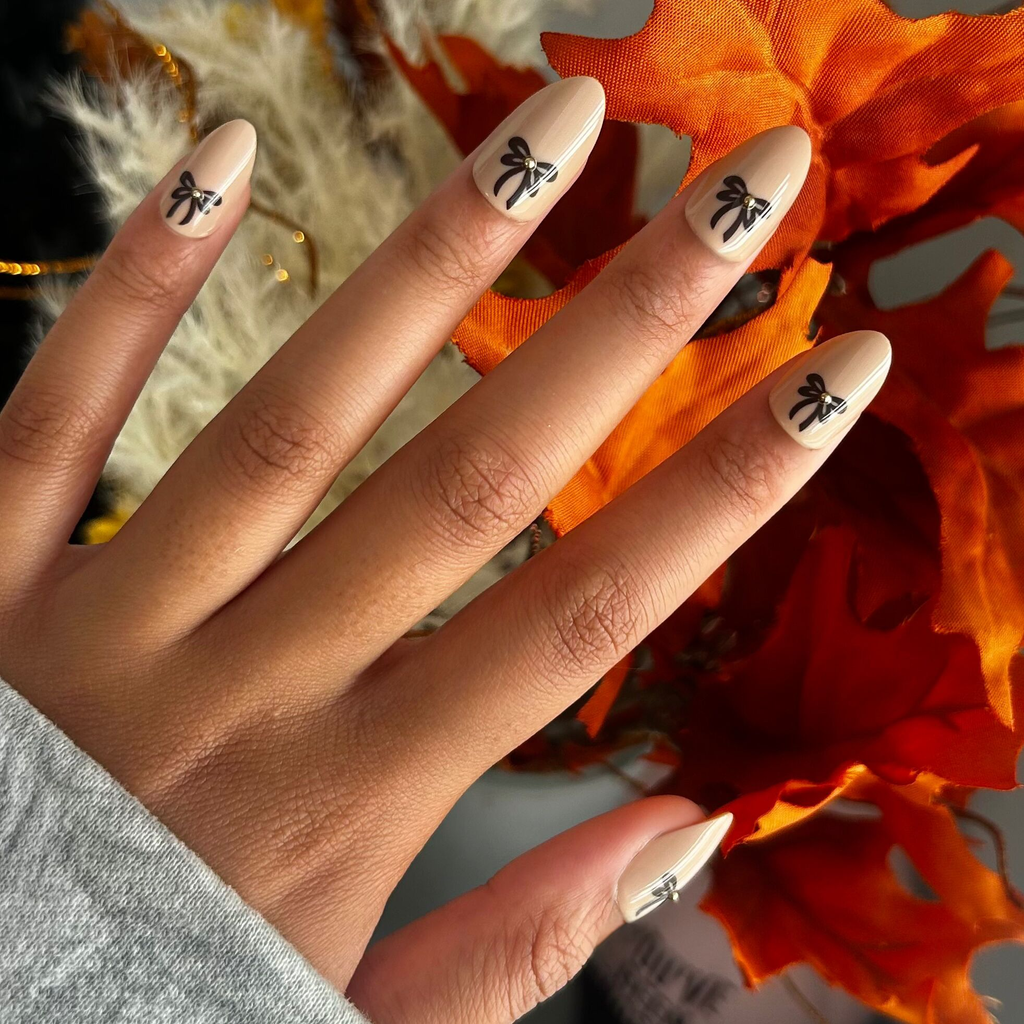 Little Gem Bows - Press On | Medium | Almond nails with creamy beige polish, black bow designs, and 3D puffy gems for an easy mani
