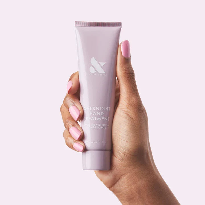 Hand holding a tube of Hand Treatment Duo with glossy pink manicure on natural nails against pale pink background