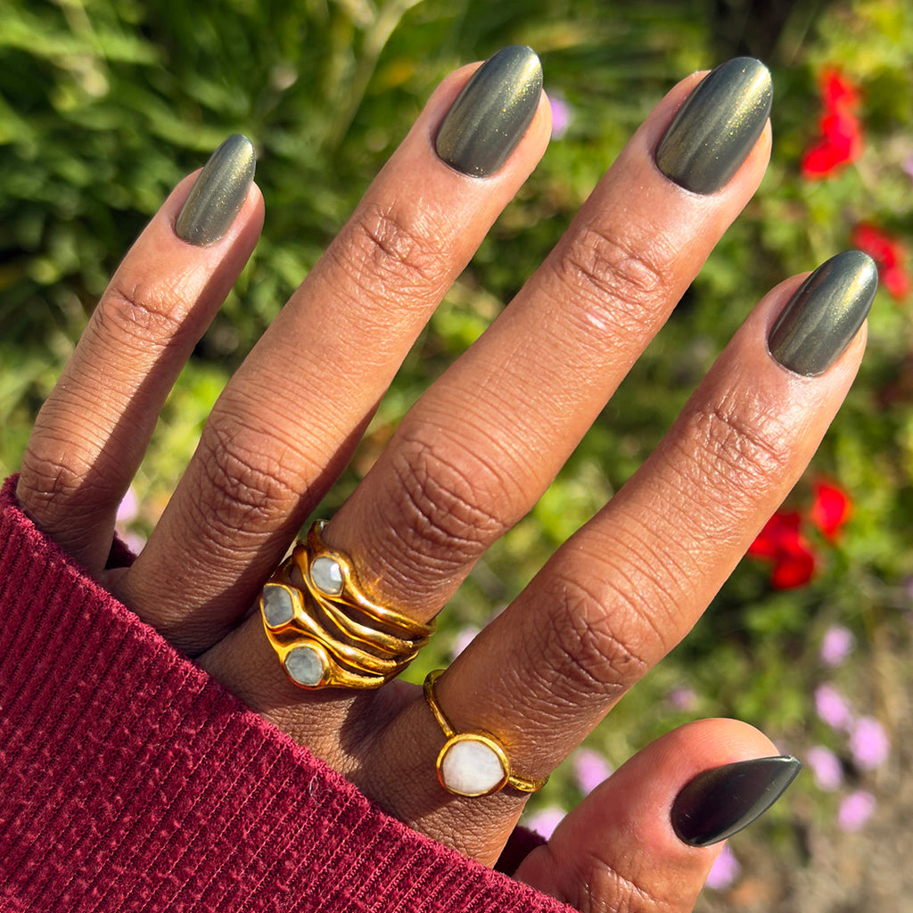 Hand wearing gold rings with medium oval nails in Martini Chrome - Press-On | Medium | Oval deep olive green polish