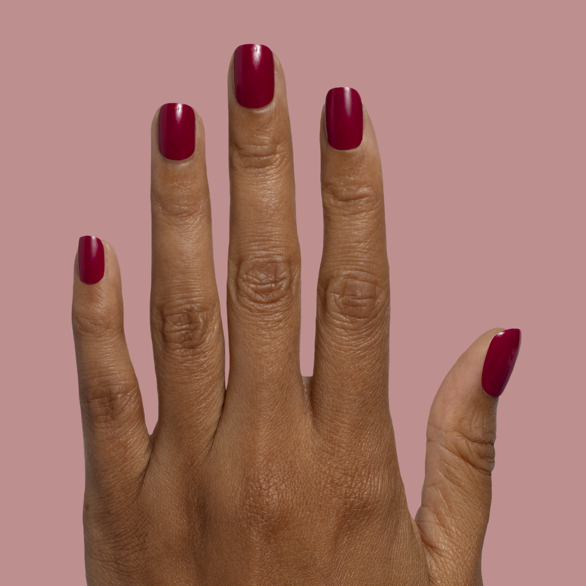 Mulberry | Extra Short | Squoval - Tab Press-On deep mulberry press-on nails on hand against muted pink background
