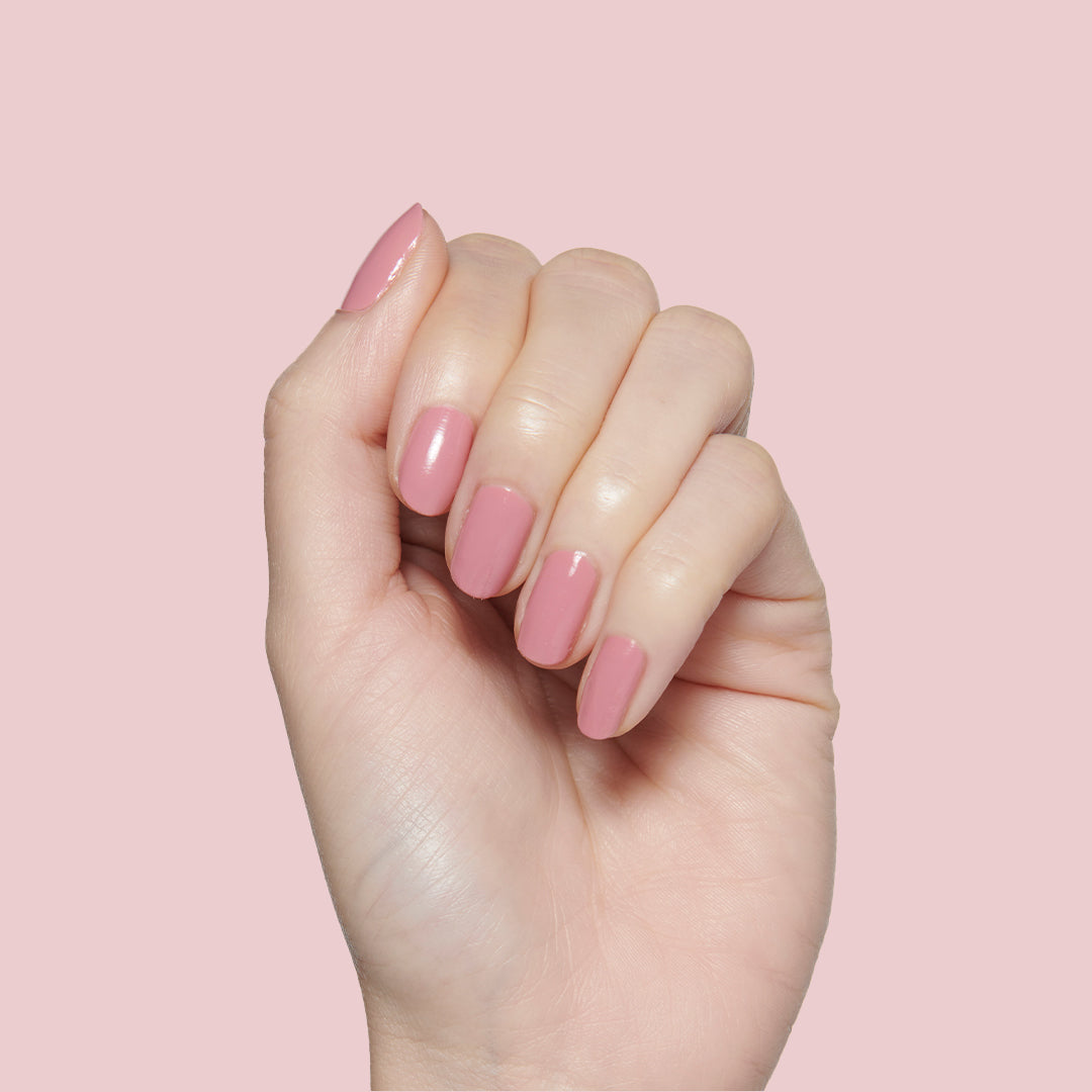 Hand with glossy nails painted in dusty rose pink Yogurt Parfait polish on pale pink background for mani or pedi