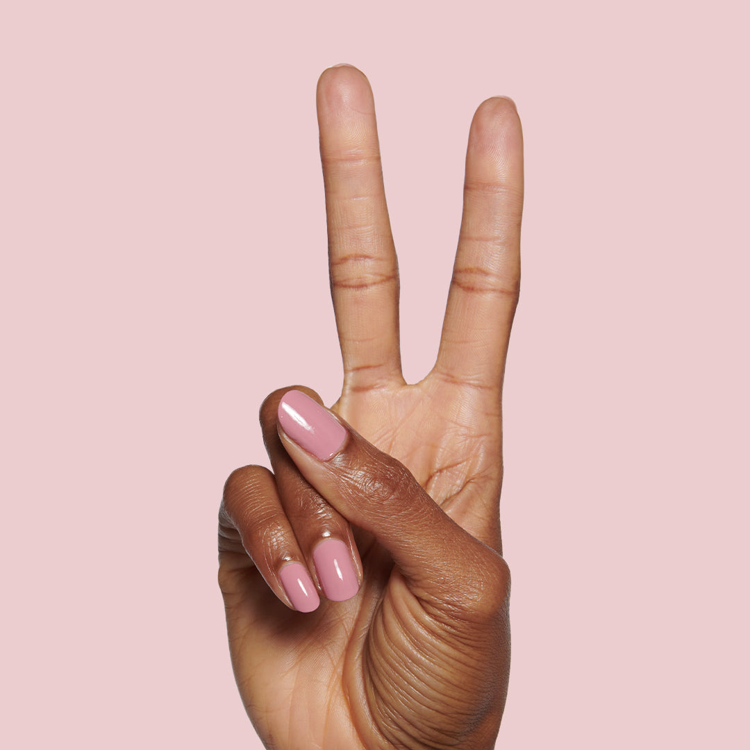 Hand with glossy nails painted in dusty rose pink Yogurt Parfait polish holding two fingers up on pink background
