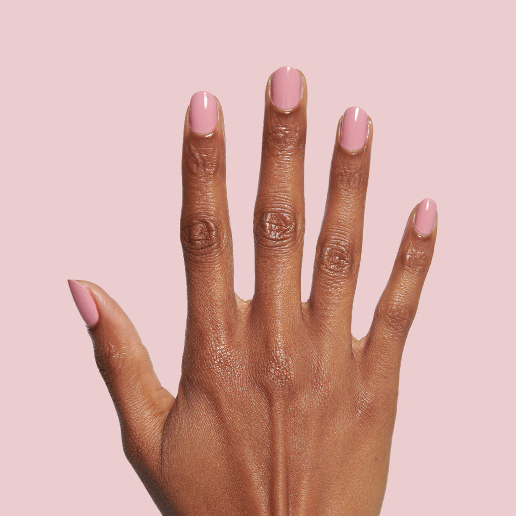 Hand with smooth nails painted in dusty rose pink Yogurt Parfait polish against pale pink background