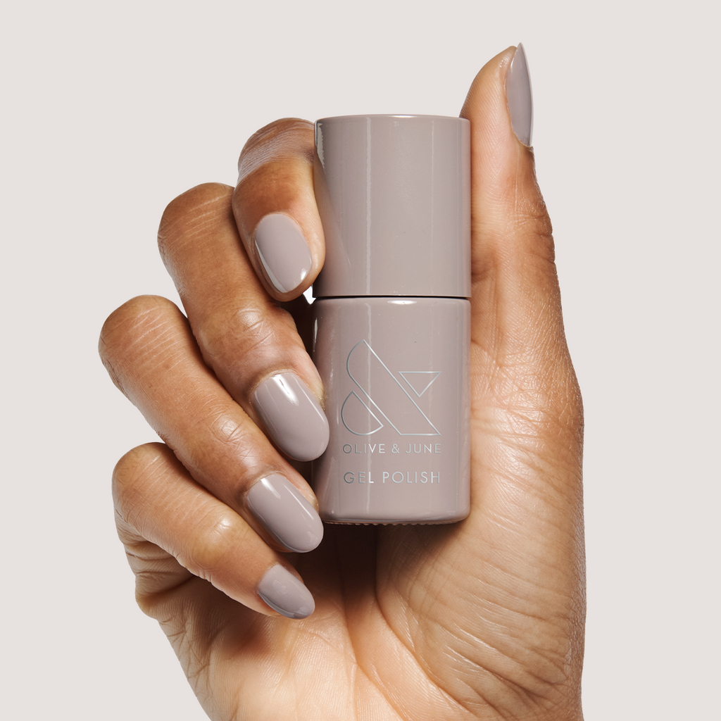 Hand holding AW - Gel bottle with warm toned grey gel polish manicured nails on neutral background