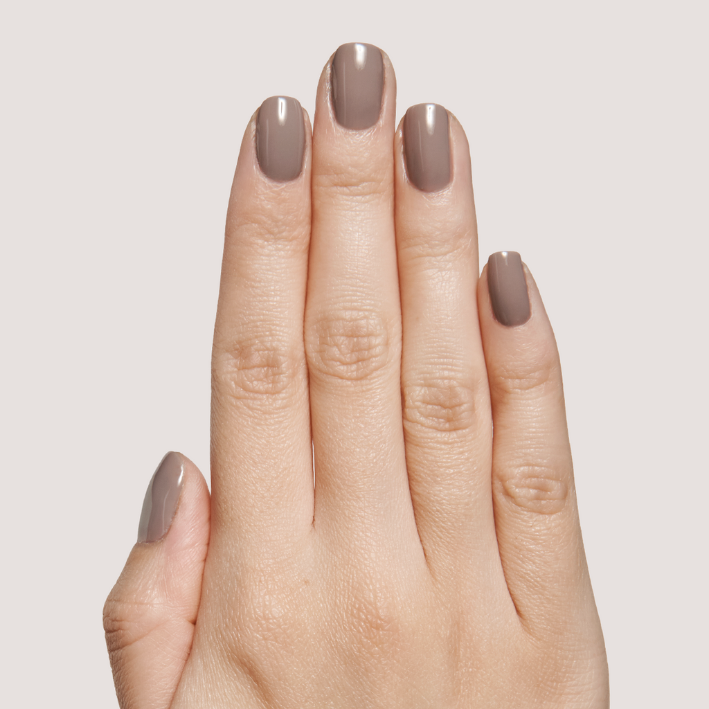 Hand with nails painted in AW - Gel warm grey polish for a smooth, long-lasting manicure on neutral background