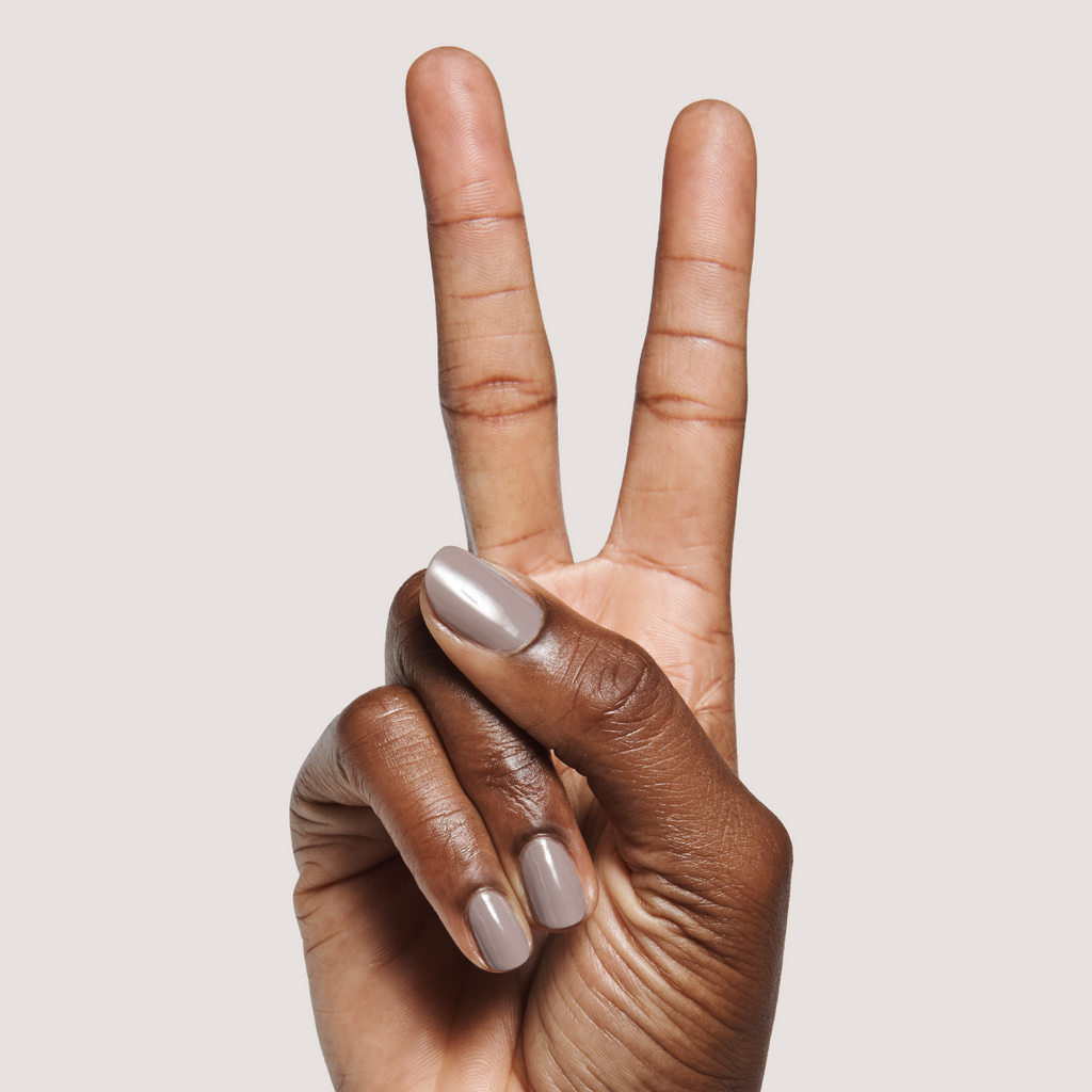 Hand with short rounded nails painted in AW - Gel warm toned grey for a polished long-lasting manicure on neutral background