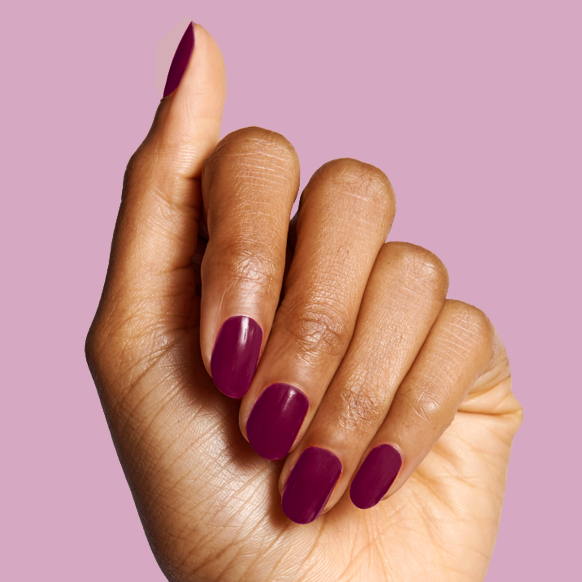 Hand with rounded nails painted in deep mulberry purple Plaza gel polish against lavender background