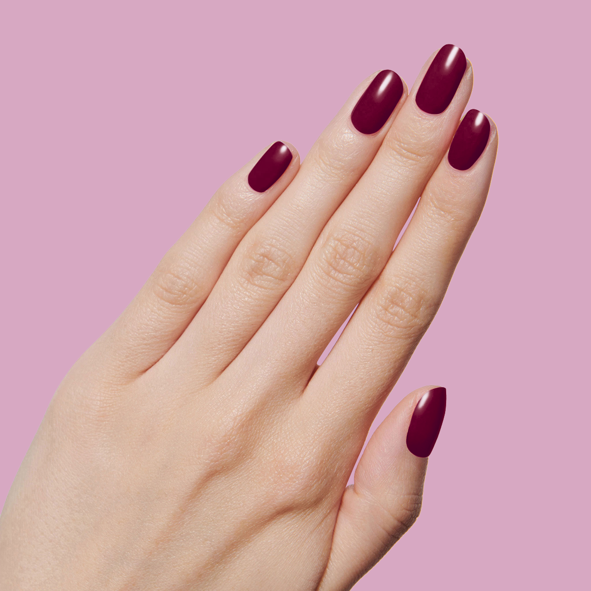 Hand with smooth nails coated in deep mulberry purple Plaza polish against soft pink background