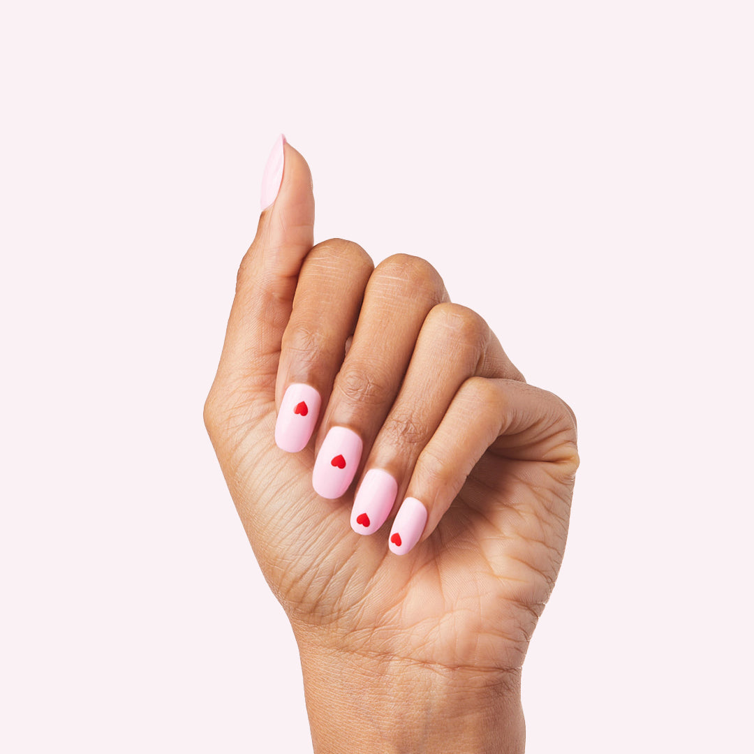 Pink Perfect Heart - Press-On | Round | Short with soft pink base and small red hearts nail design on hand against light background