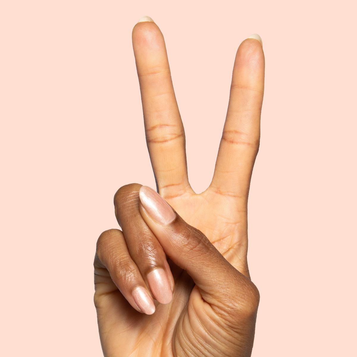 Cookie Swap Gel shimmery beige champagne gel polish on natural nails shown in a peace sign manicure by Olive and June