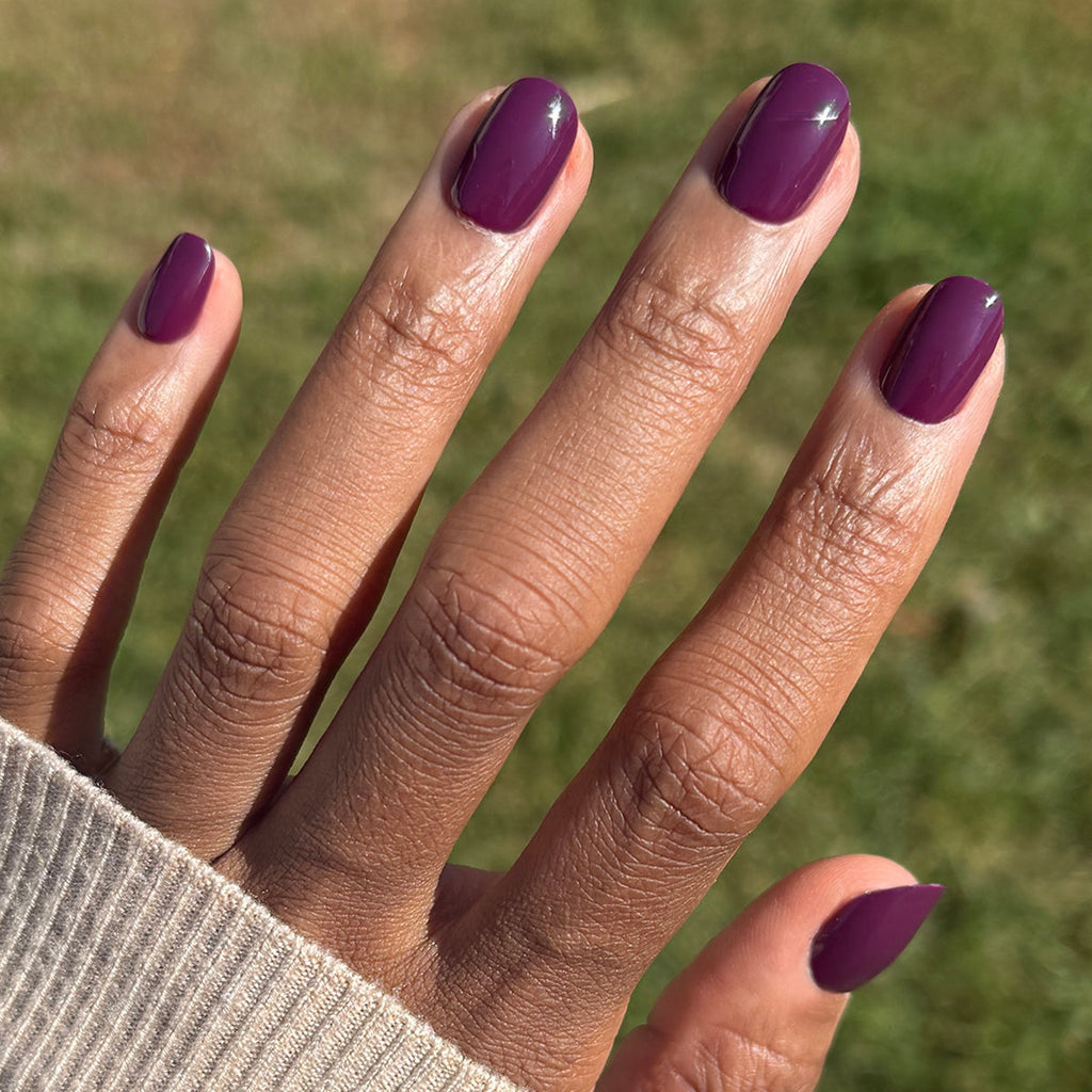 Hand with short round press-on nails in dark purple shade Who Likes Raisins? - Press-On | Extra Short | Round outdoors in sunlight