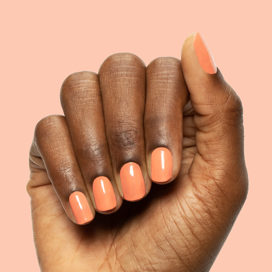 Hand with medium-length nails painted in coral Ride into the Sunset gel polish against soft peach background