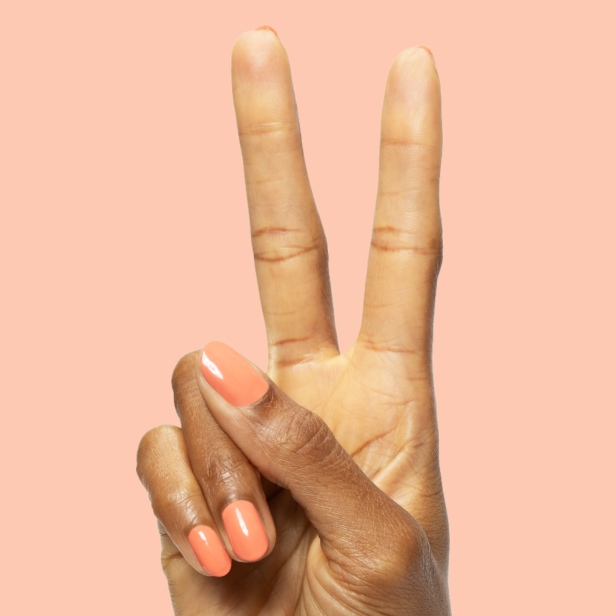 Hand with medium nails painted in coral Ride into the Sunset gel polish showing peace sign on peach background
