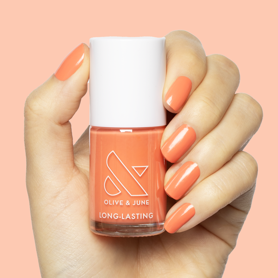 Hand holding Olive and June Ride into the Sunset polish with coral shade mani on medium-length nails