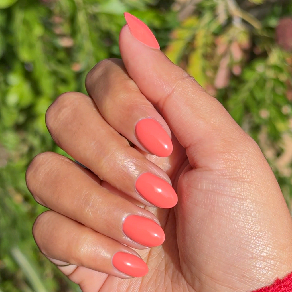 Hand with almond-shaped nails painted coral Ride into the Sunset gel polish in natural light outdoors