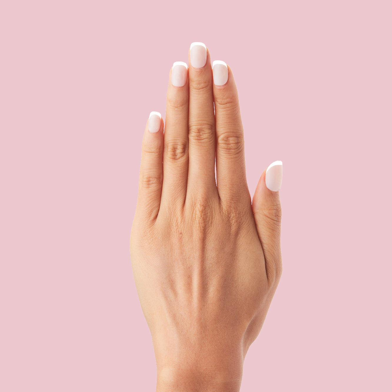 Classic French - Press-On | Extra Short | Squoval nails with neutral peachy pink base and crisp white tips on hand against pink background
