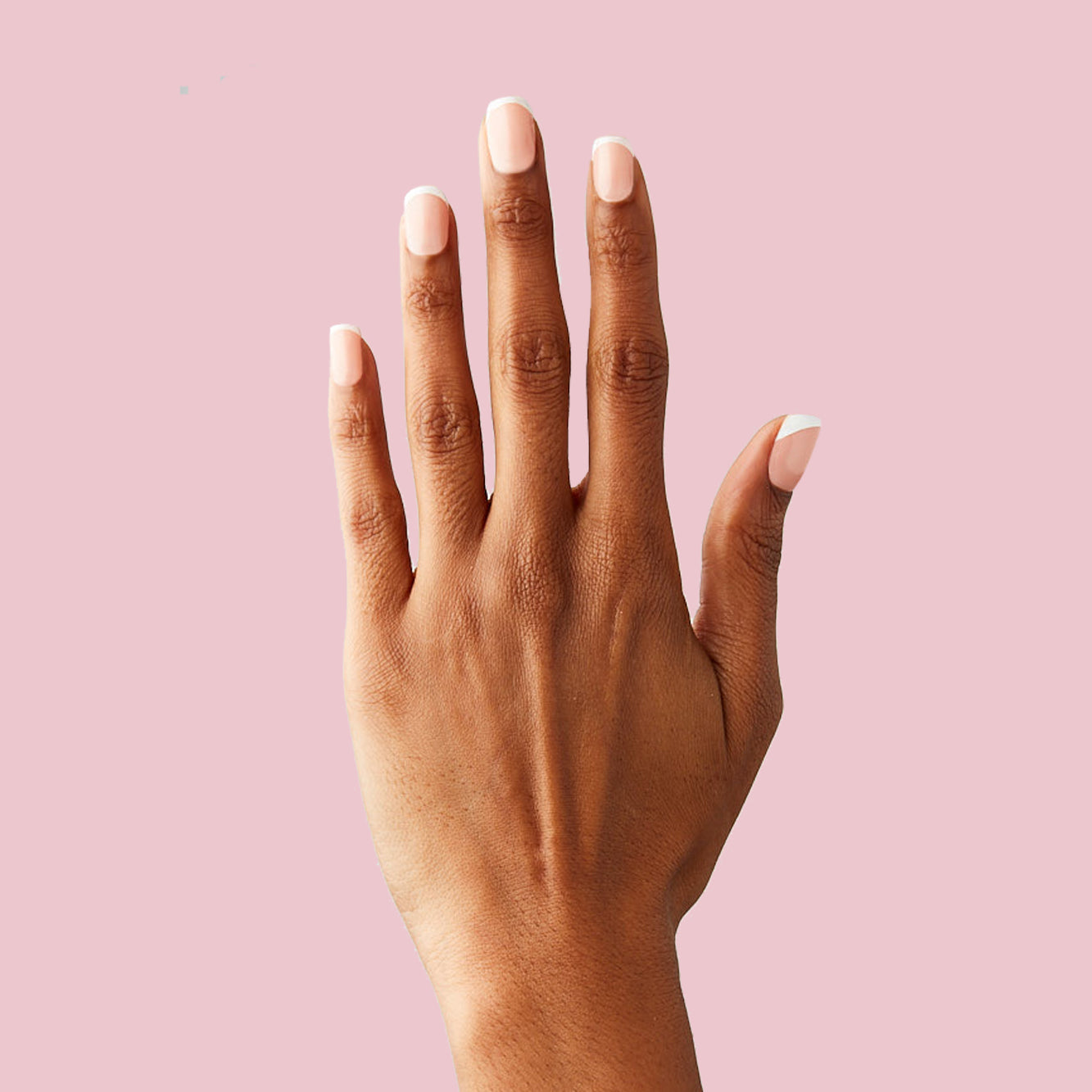 Classic French - Press-On | Extra Short | Squoval natural peachy pink base with sharp white tips on hand against soft pink background