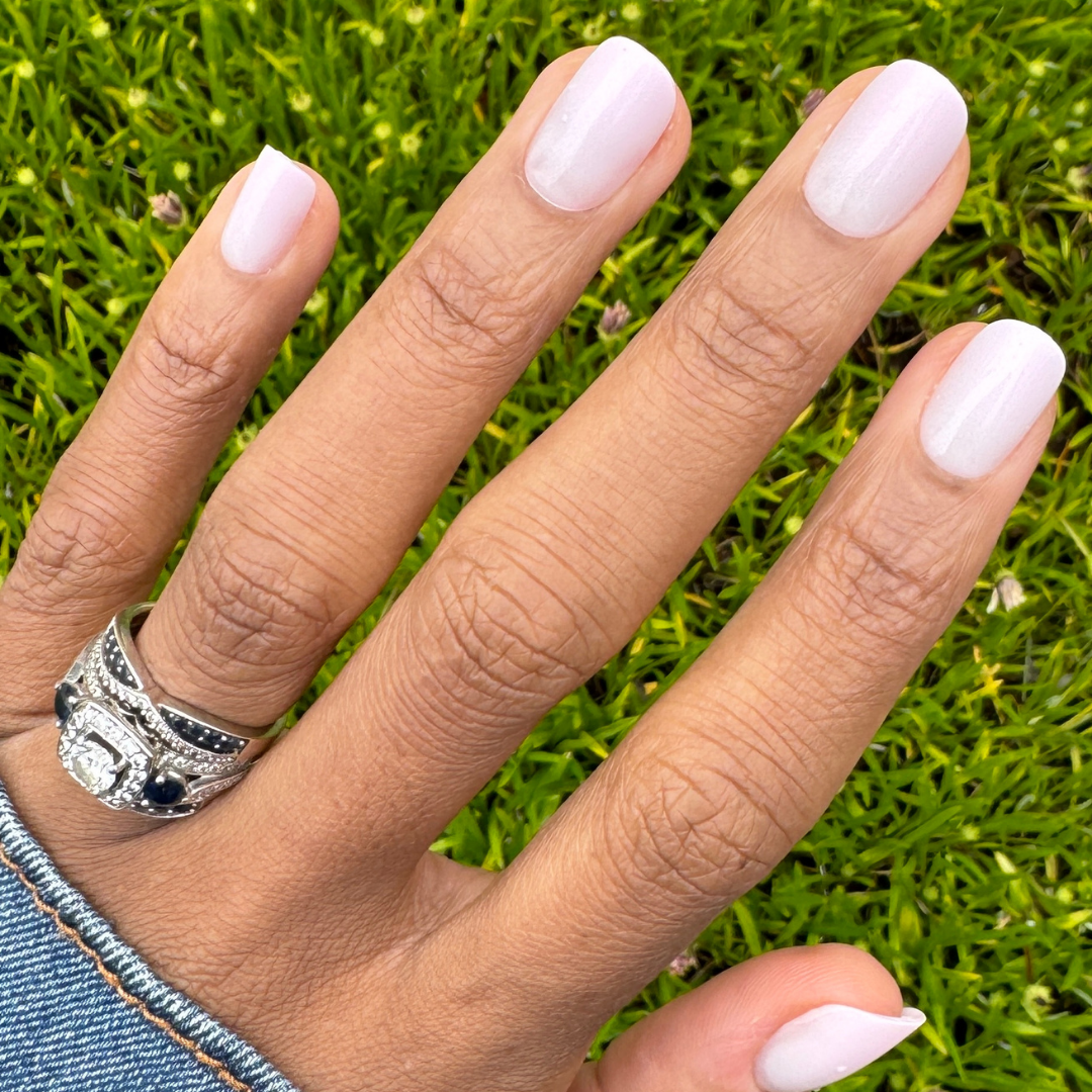 Sheer Pink Gradient - Press-On | Short | Squoval showing hand with short squoval nails in soft cool pink gradient manicure on grass background