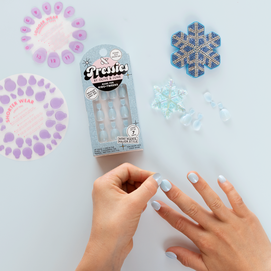 Snow Day - Pressies | Extra Short Short | Round showing pale blue press-on nails being applied with snowflake decor nearby