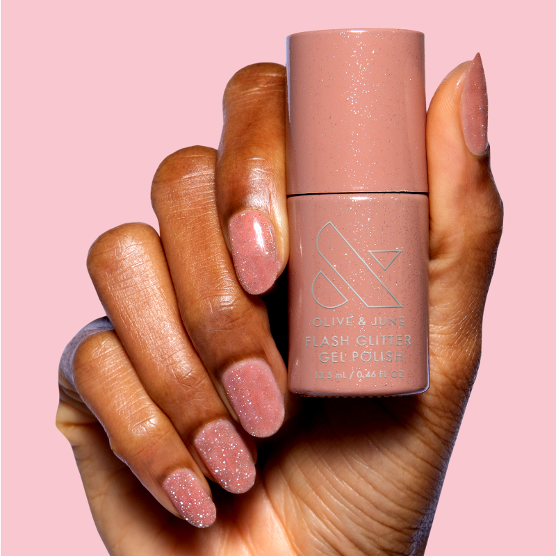 Hand holding Sparkly Pink Drink Gel polish bottle showing glittery blush pink gel manicure nails on soft pink background