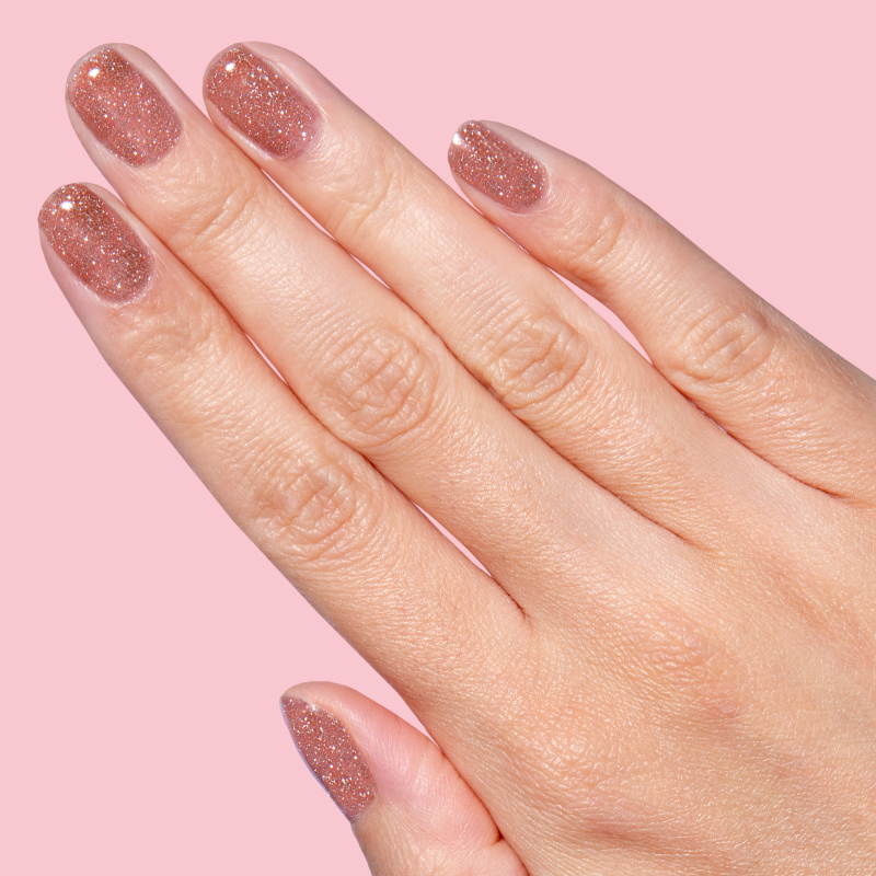 Hand with nails painted in glittery blush pink gel polish using Sparkly Pink Drink Gel on pink background