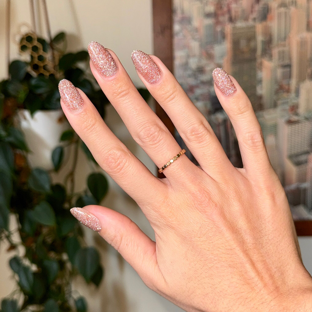 Hand with nails coated in Sparkly Pink Drink Gel showing glittery blush pink gel polish manicure with gold ring