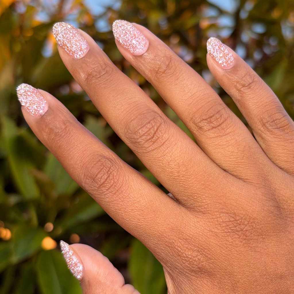 Hand with almond shaped nails painted with glittery blush pink manicure using Sparkly Pink Drink Gel polish