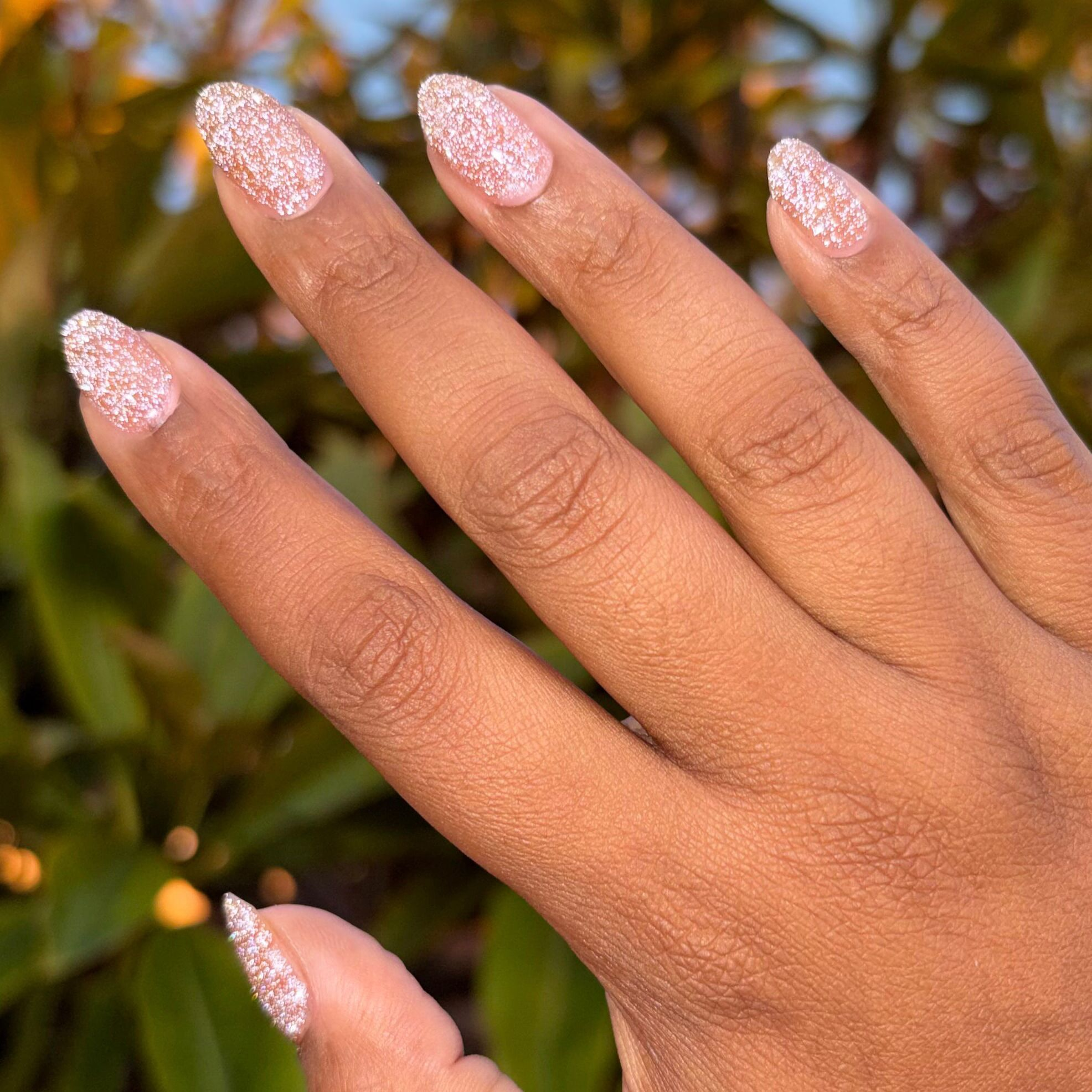 Hand with almond shaped nails painted with glittery blush pink manicure using Sparkly Pink Drink Gel polish