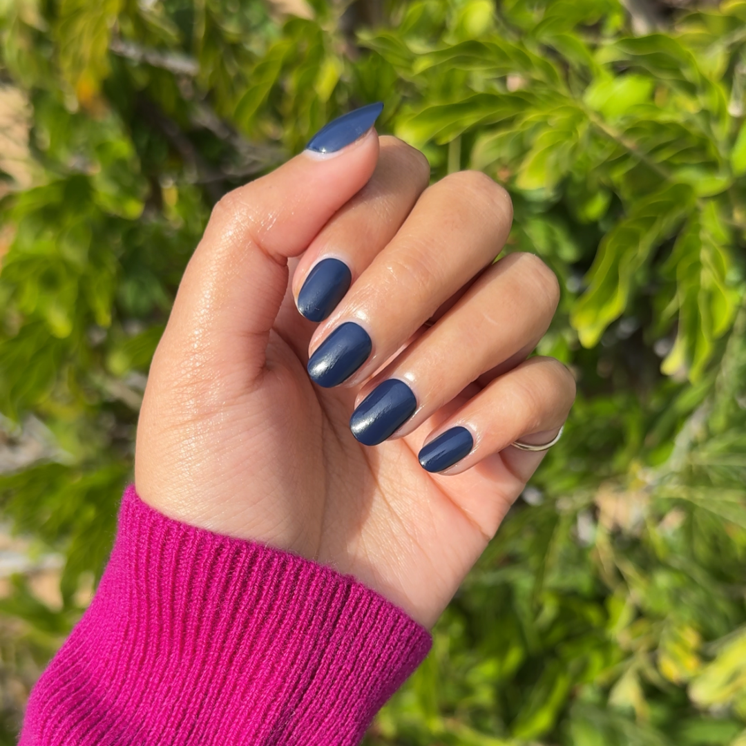 Suited | Extra Short | Round - Tab Press-On showing hand with dark sapphire quick dry press-on nails outdoors in pink sweater