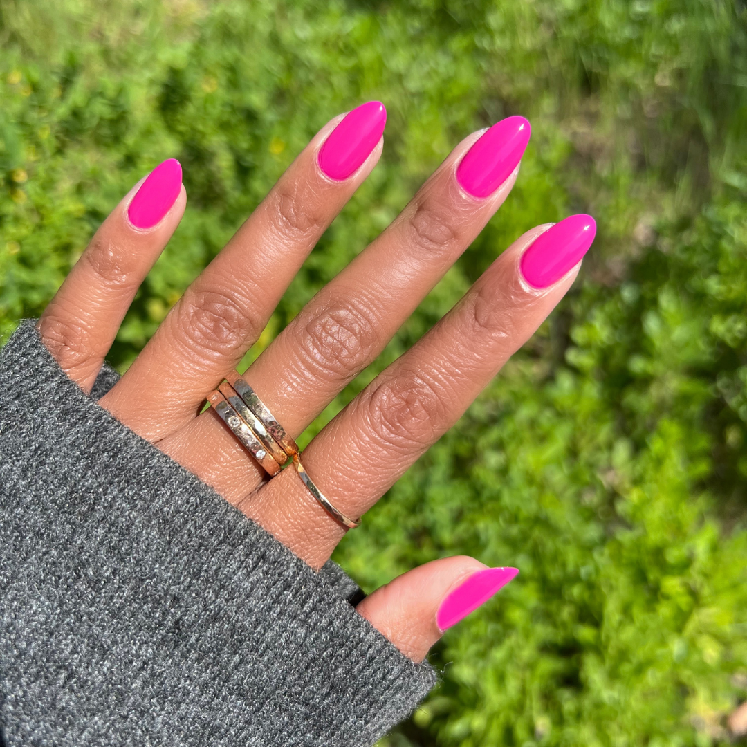 Hand with long almond-shaped nails painted in bright orchid magenta Wildest gel polish against green outdoor background