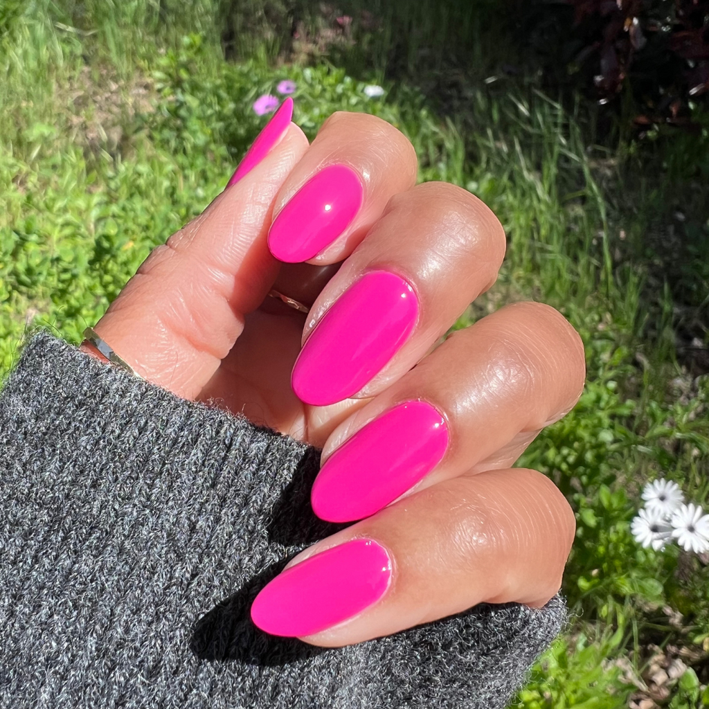 Hand showing glossy bright orchid magenta Wildest gel polish on medium-length nails outdoors with greenery background