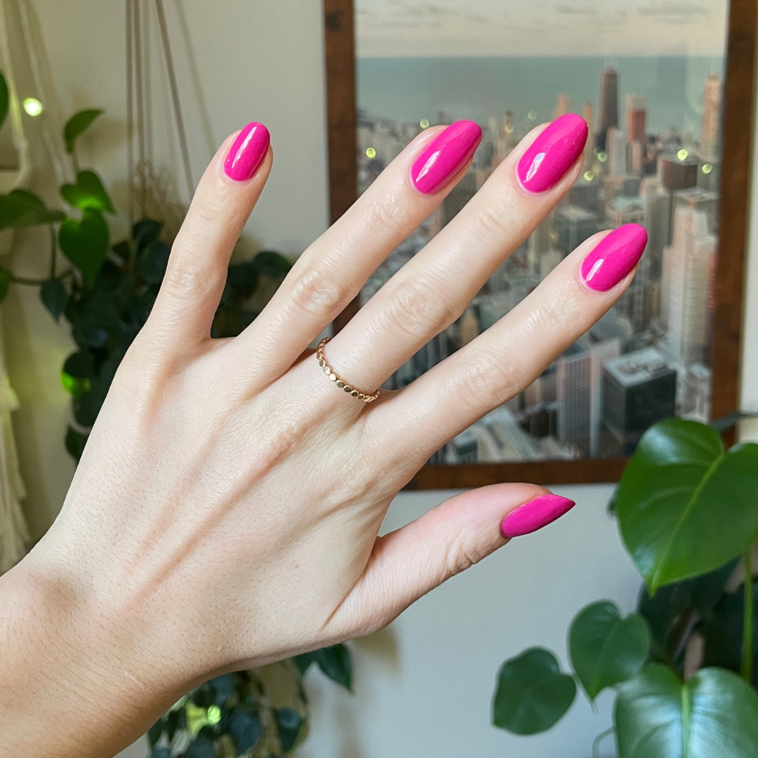 Hand with medium-length nails painted in bold orchid magenta Wildest gel polish with gold ring indoors by plants and city photo