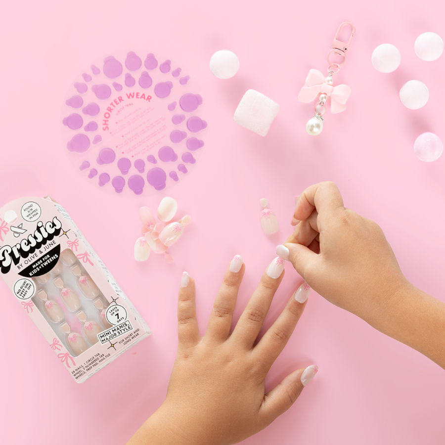 Wrapped in Pink - Pressies | Short Medium | Round showing child placing baby pink french press-on manicure with 3D bow detail