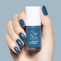 Hand holding Bodysuit gel polish bottle with matching teal quick-dry manicure on medium-length natural nails against blue background