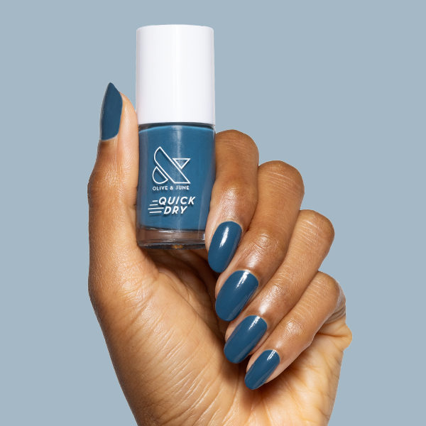 Hand holding Bodysuit quick-dry gel polish bottle with matching deep teal manicure on medium-length nails against blue background