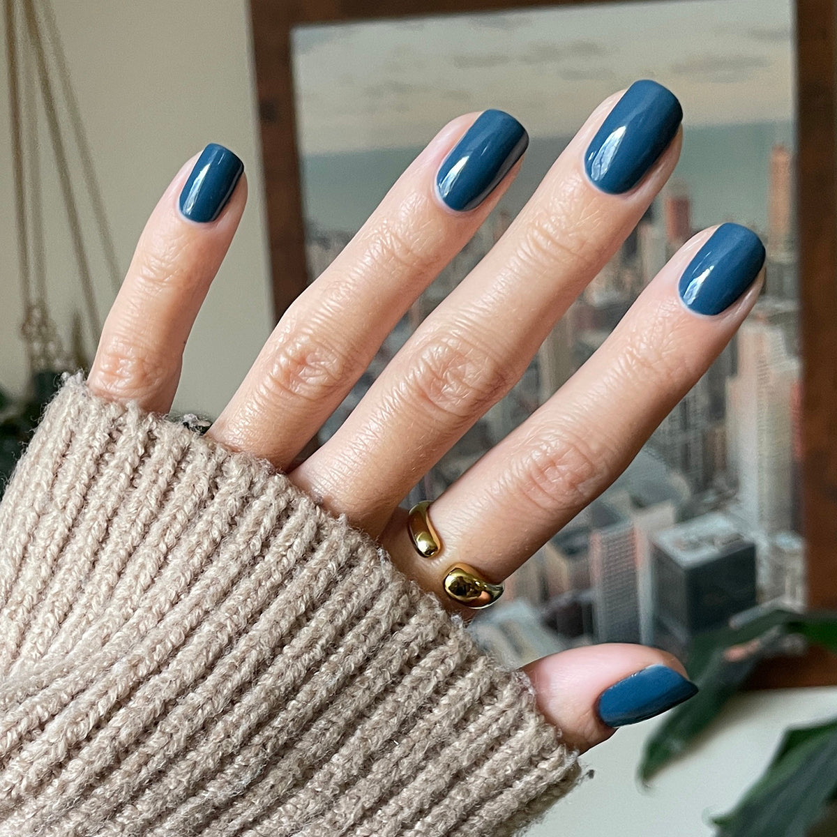 Hand with Bodysuit gel polish manicure in dusty cool teal on medium-length nails against blurred cityscape background