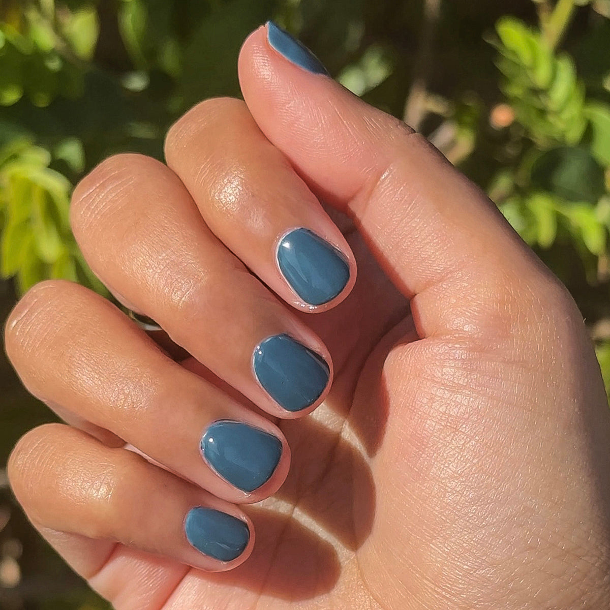 Hand with Bodysuit gel polish manicure in dusty cool teal shade on short natural nails in outdoor sunlight setting