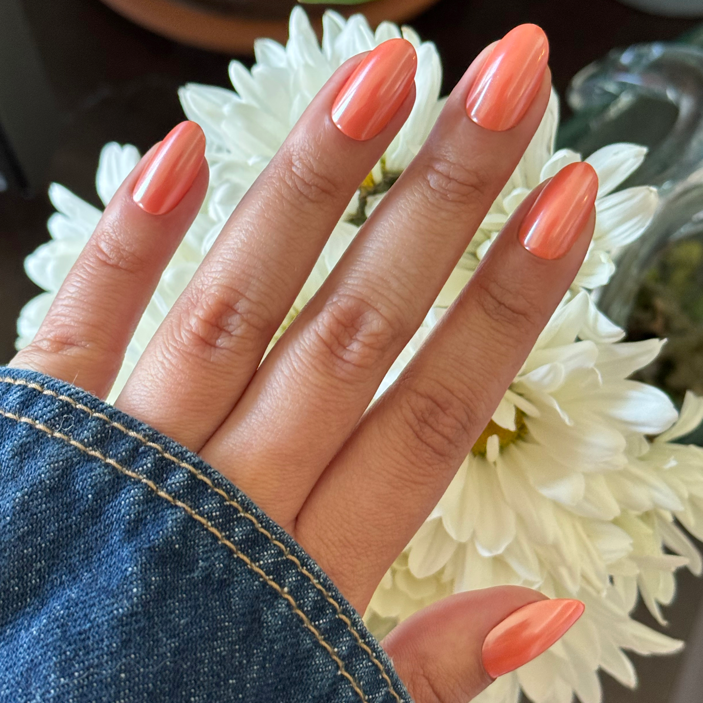 Bounce Back Chrome - Press-On | Medium | Oval bright tangerine orange oval press-on nails with chrome shimmer on hand by white flowers