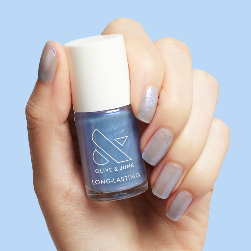 Hand holding Olive and June nail polish bottle with nails painted in cool lavender-blue sheen of Friend or Anemone? mani