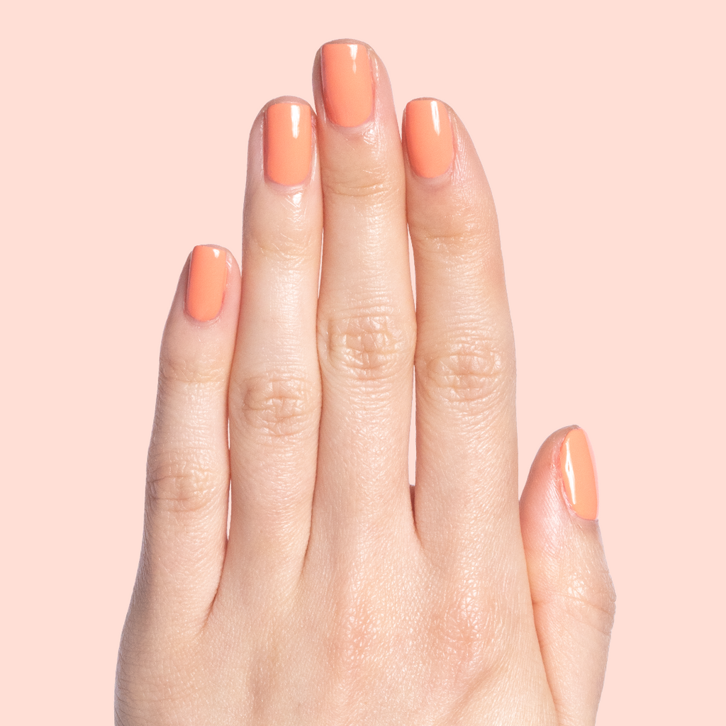 Hand with nails painted in glossy Melon quick dry polish in a soft cantaloupe shade on light peach background