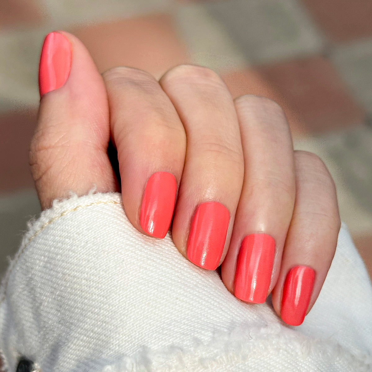 Hand with medium-length nails painted bright coral Ride into the Sunset gel polish in natural light outdoors