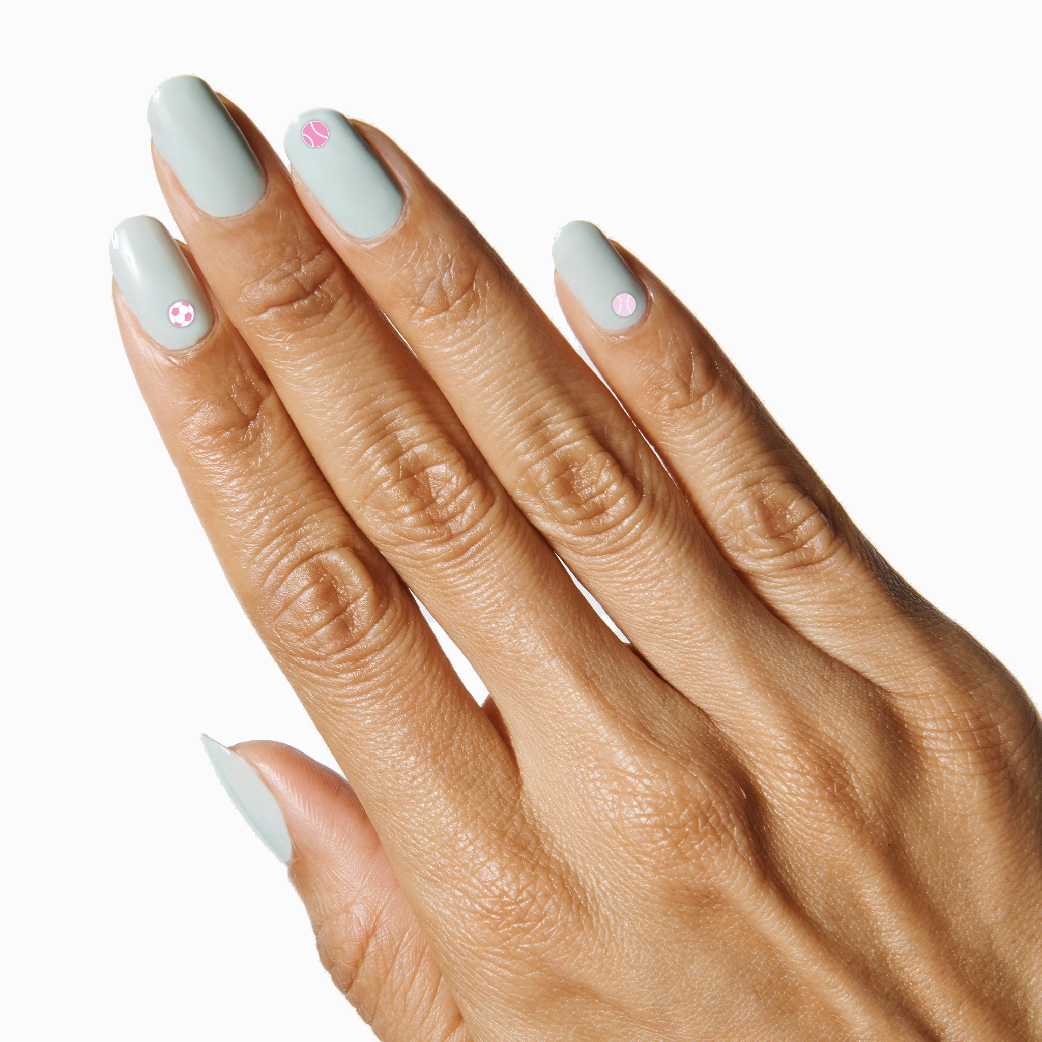 Hand with soft grey polish and tiny pink Sports Pack nail stickers showcasing sporty icons for a fun manicure