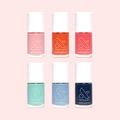 Six colorful nail polish bottles from the Summer Polish Set by Olive and June arranged on a pale pink background