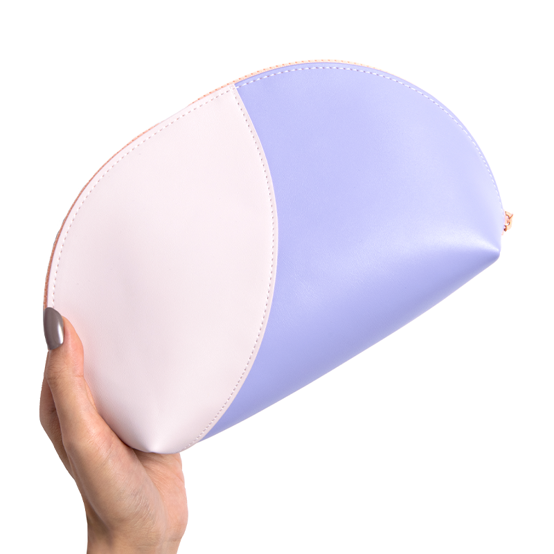 Hand holding a pastel purple and pink vegan leather Travel Pouch with curved design on white background