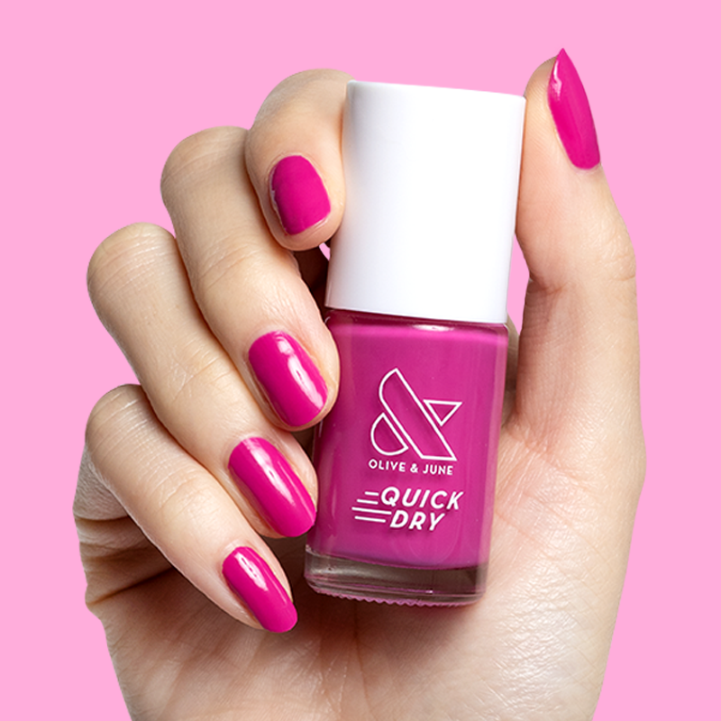 Hand with nails painted in bold orchid magenta holding Wildest quick dry gel polish bottle against pink background