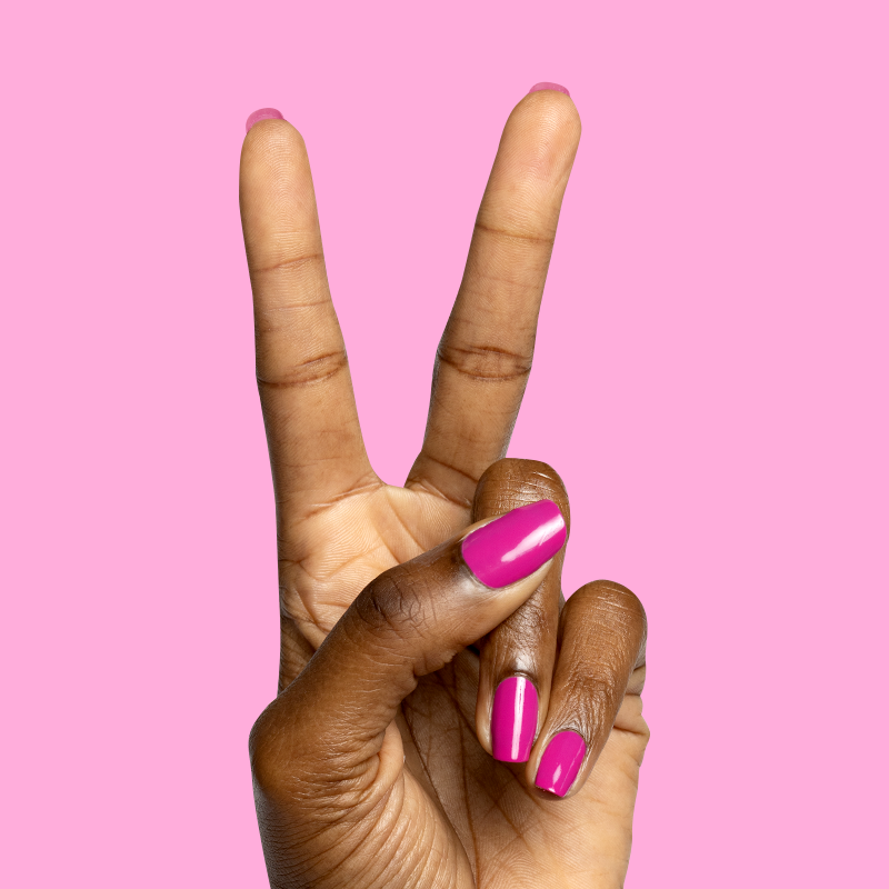 Hand with nails painted in vibrant orchid magenta Wildest gel polish showing glossy, bold mani on pink background