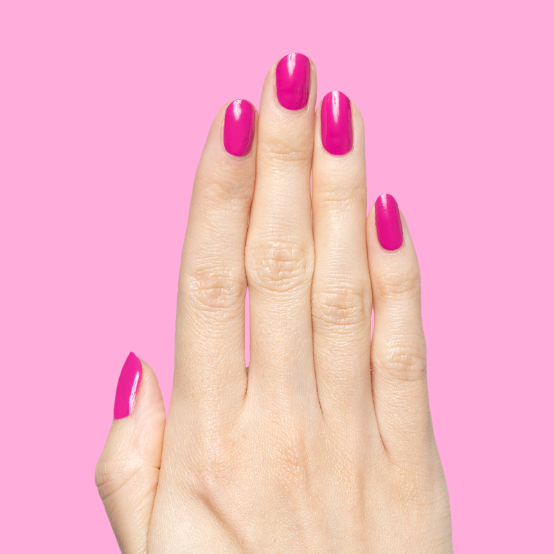 Hand with nails painted in vibrant orchid magenta Wildest gel polish showing glossy, bold manicure against pink backdrop